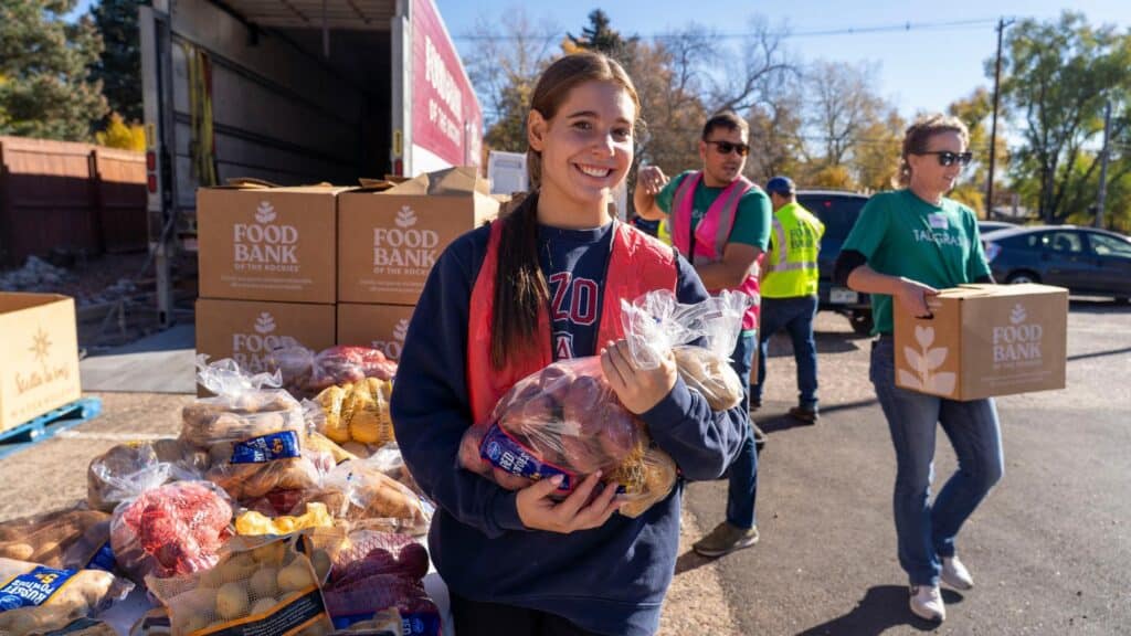 Volunteer holding bag of potatoes in front of other food, boxes, and a truck at a mobile pantry.