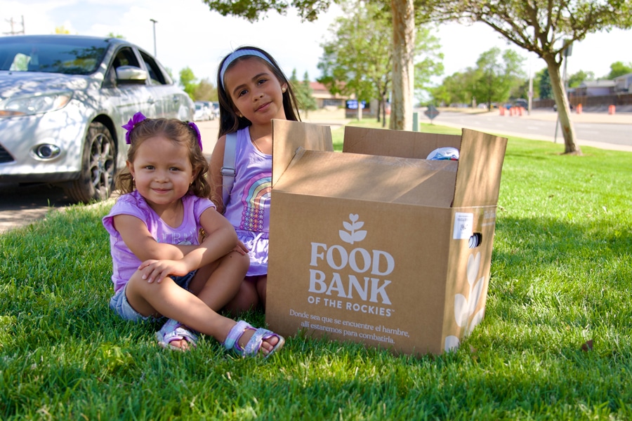 Girls sitting outside on a lawn next to a Food Bank of the Rockies food box.