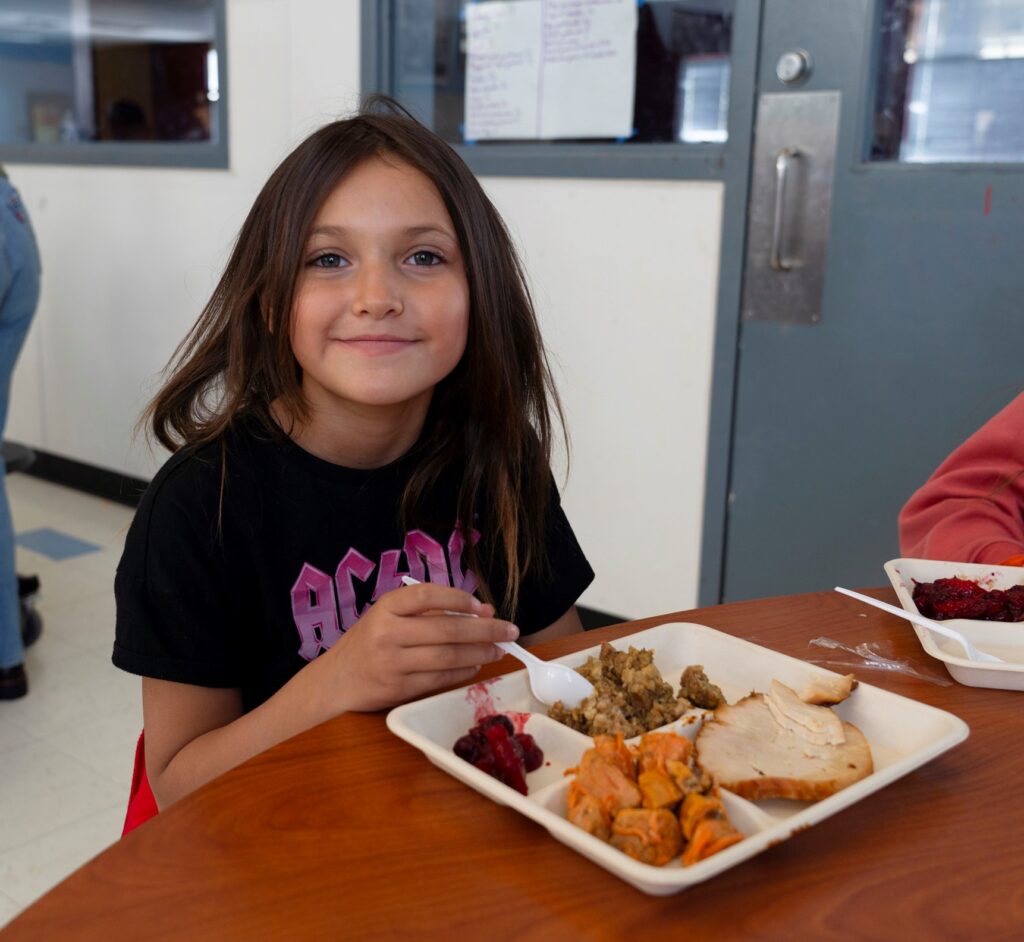 girl sitting at cafeteria table eating a tray of turkey and stuffing.
