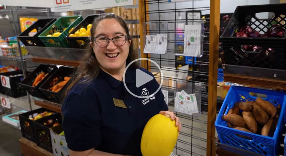 Woman smiling holding a spaghetti squash inside a warehouse with produce behind her.