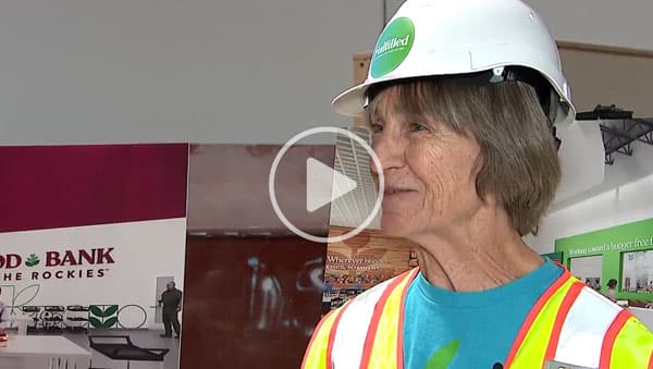 Woman standing with construction vest and hat.