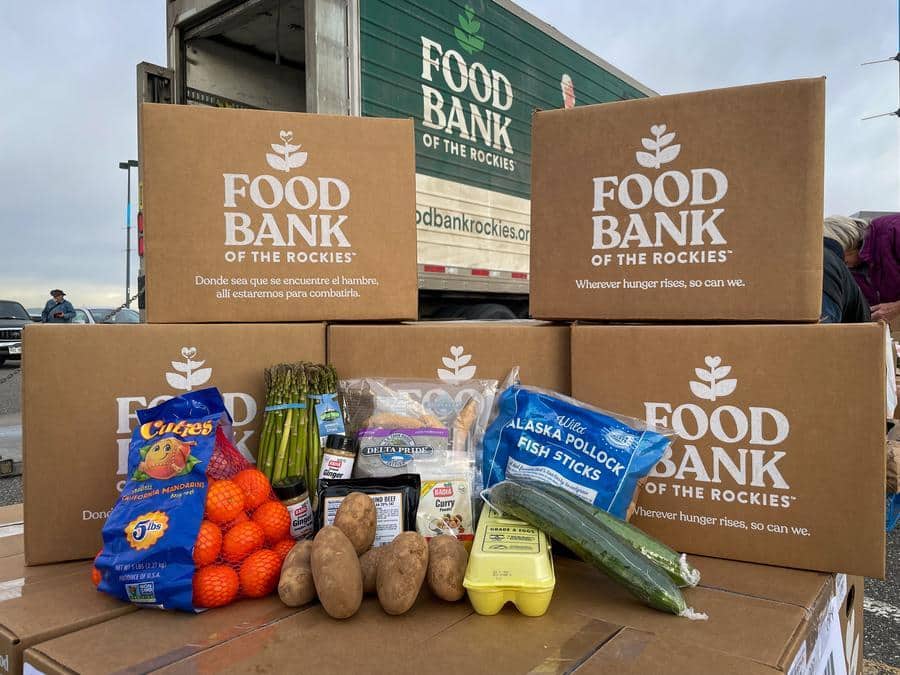 Food Bank of the Rockies boxes stacked, with produce, potatoes, eggs, and frozen fish in the foreground. Truck in the background.