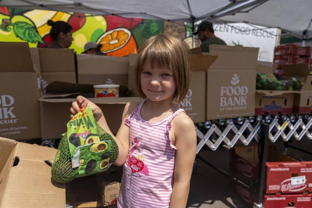Young girl holding bag of grapes under an event tent with Food Bank boxes in the background.