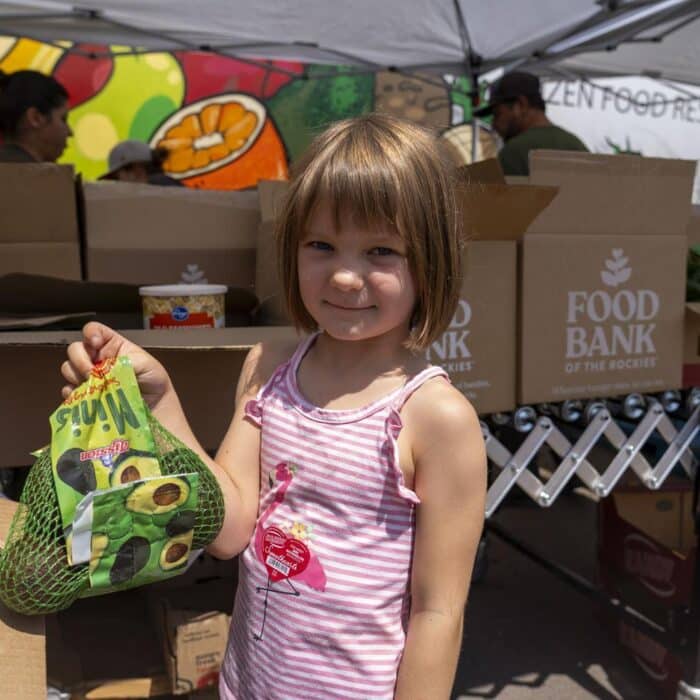 Young girl holding bag of grapes under an event tent with Food Bank boxes in the background.