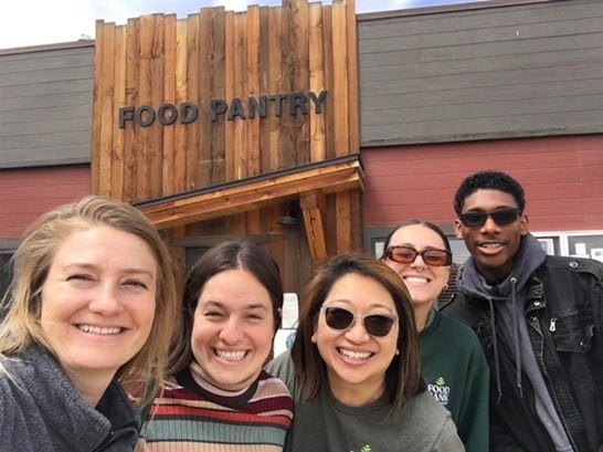 a group of smiling people standing in front of a food pantry