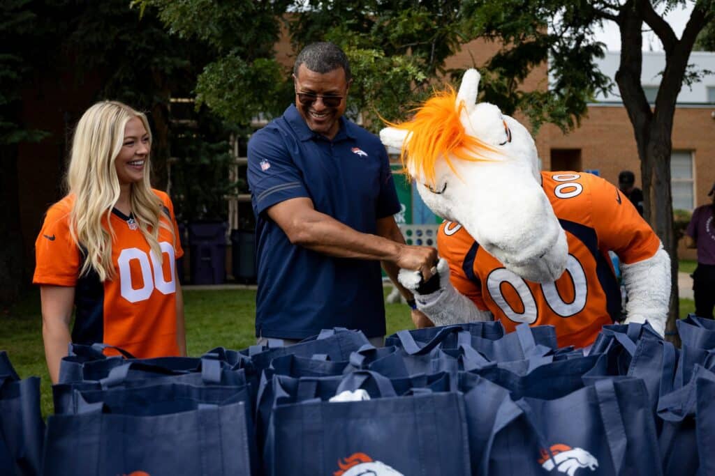 Denver Broncos staff and cheerleaders packing totes of hope for kids meals.