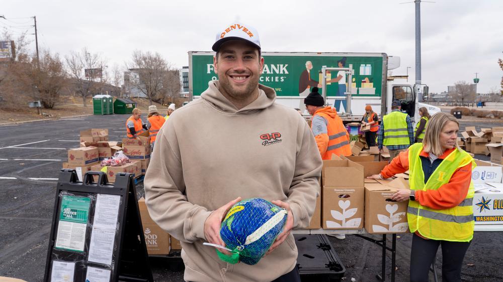 Denver Broncos Zach Allen holding frozen turkey at a food distribution.