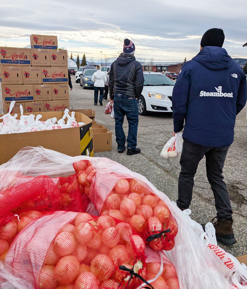 Volunteers helping to distribute food to a line of cars. Bags of onions in the foreground, boxes in background.