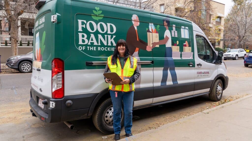 Peggy wearing safety vest standing in front of Food Bank of the Rockies van.