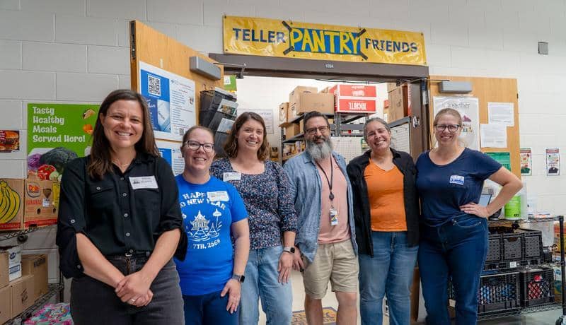 Staff and volunteers standing in front of food pantry. Sign above the doorway says Teller Pantry Friends.