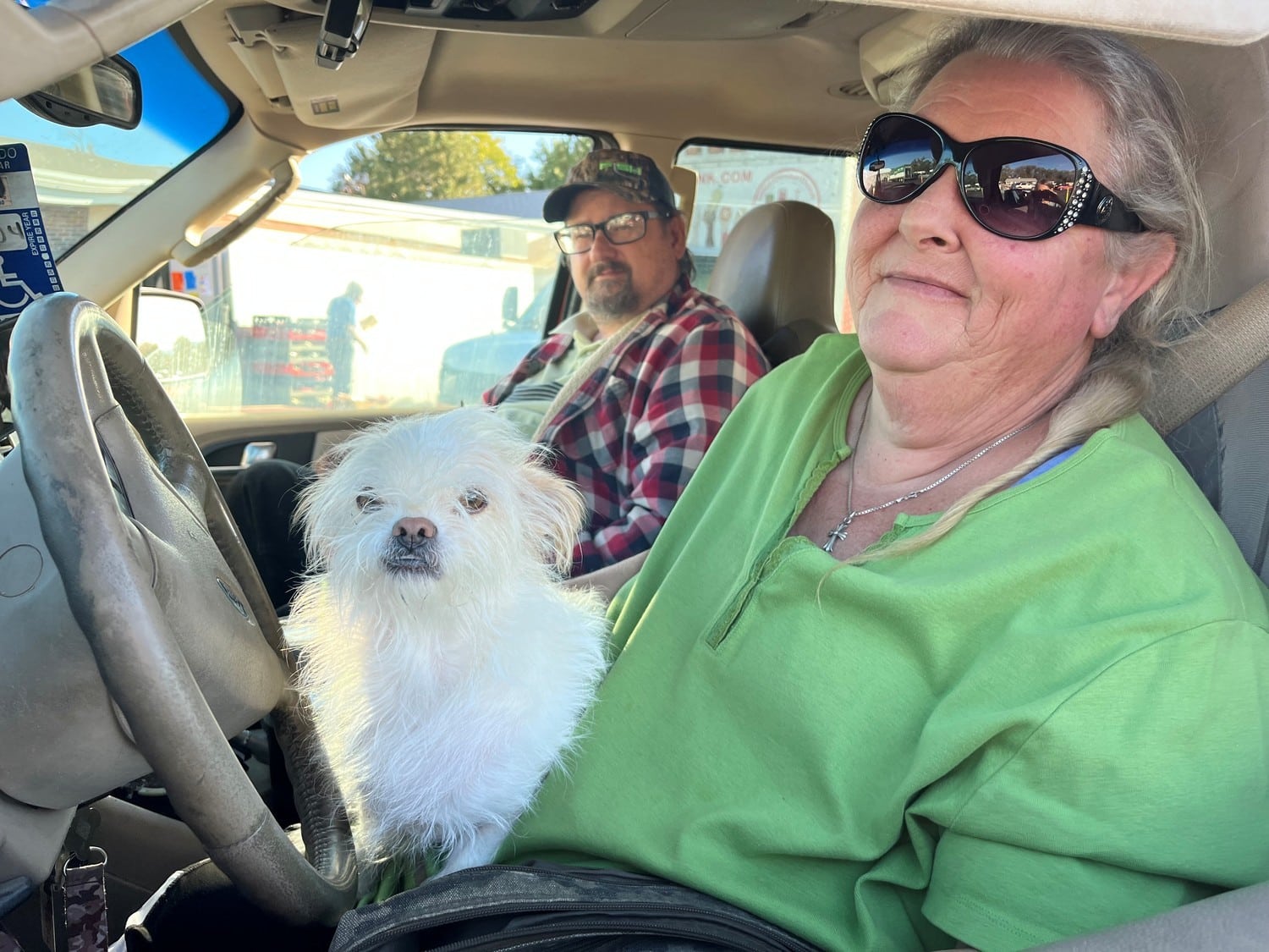 Man and woman and a white dog sit in the front of a car.