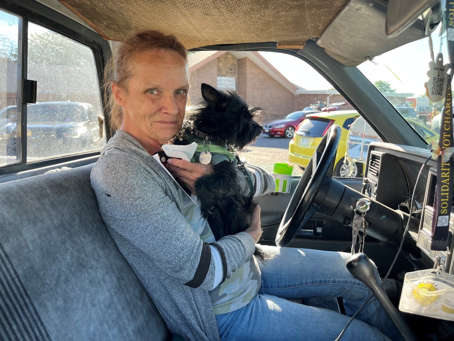 Lori holding black dog sitting in front of a car.