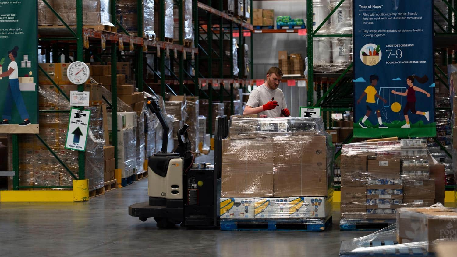 staff person marking a pallet of produce boxes inside a warehouse.