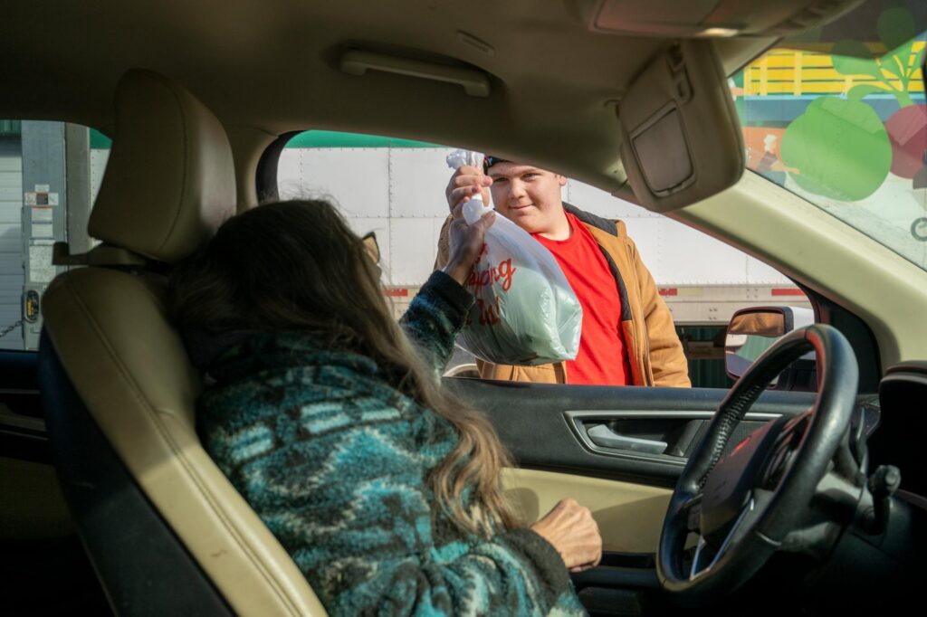 volunteer hands bag of produce to woman sitting in a car.