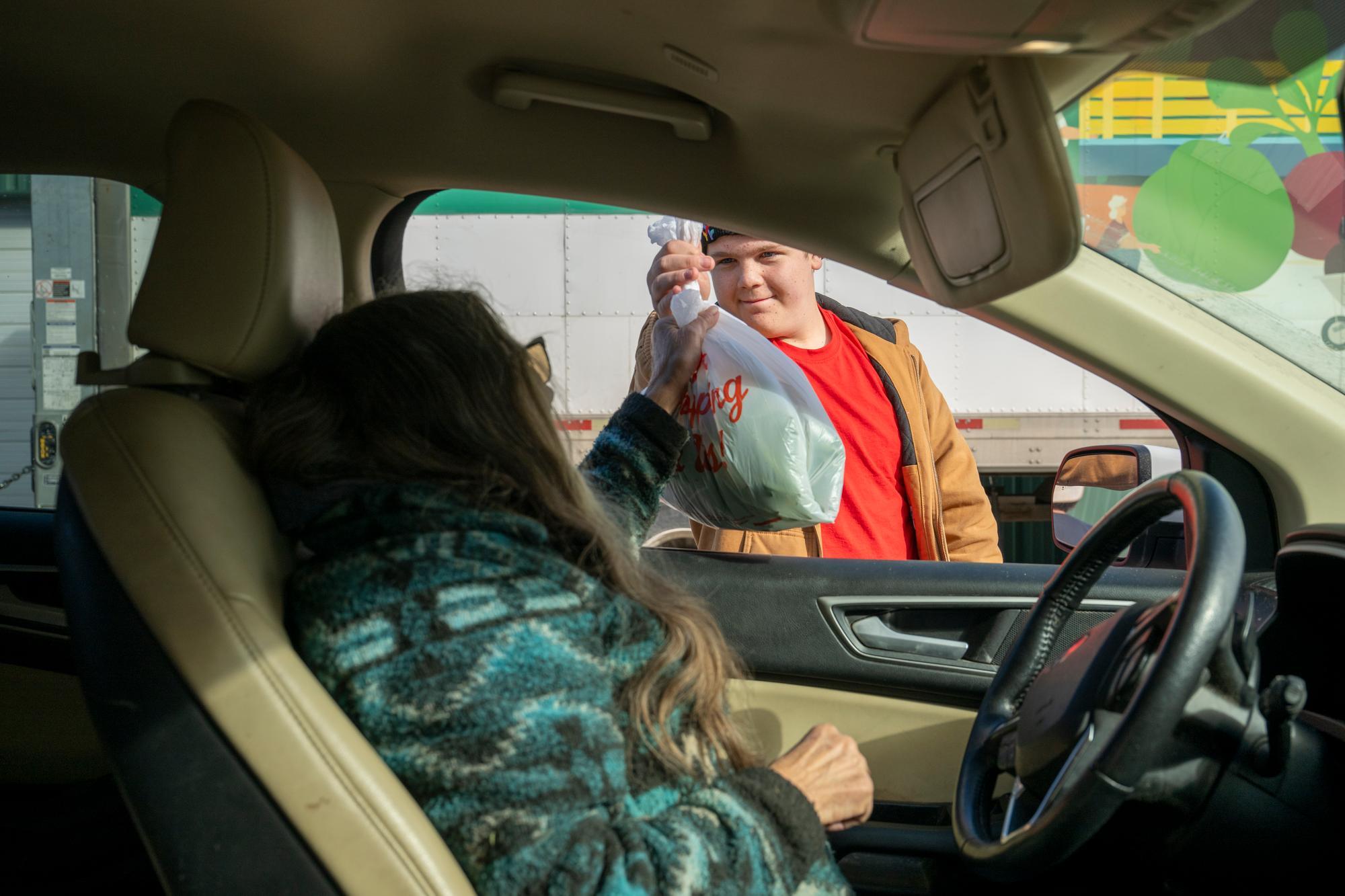 volunteer hands bag of produce to woman sitting in a car.