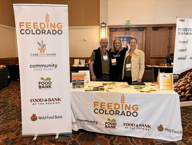 Feeding Colorado team members standing behind a table with Feeding Colorado signage
