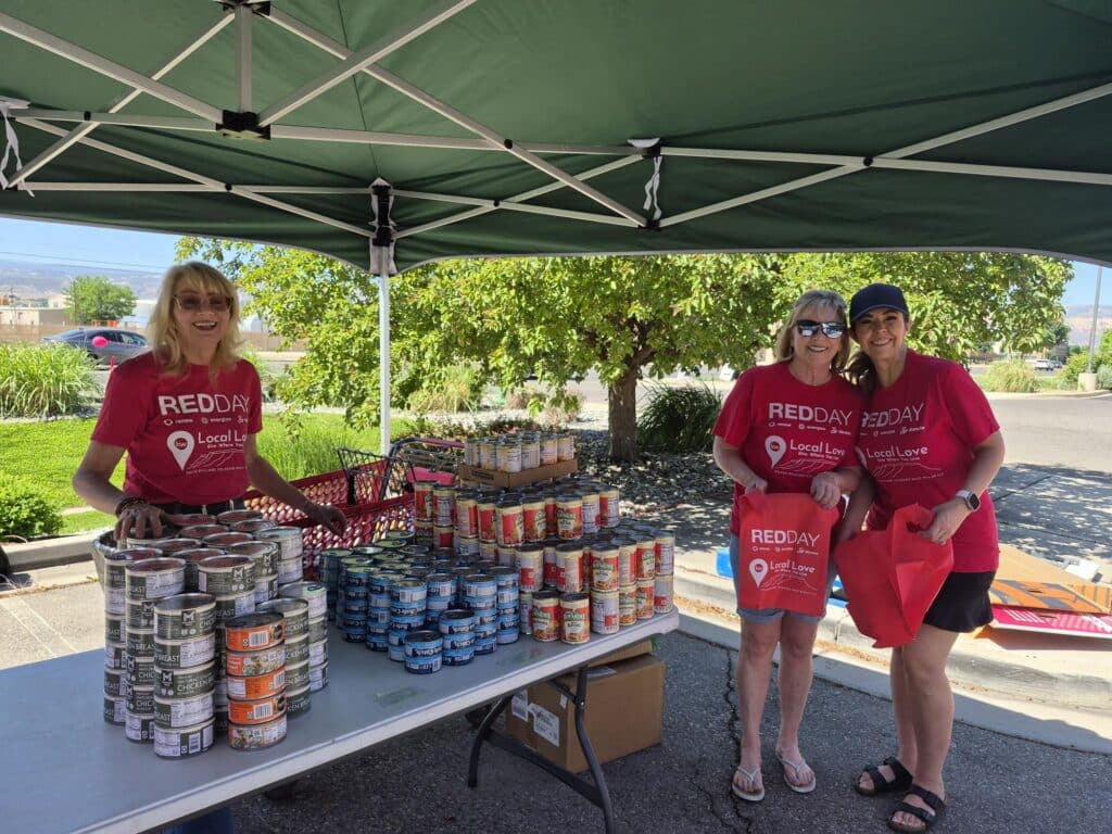 Three Keller Williams volunteers standing under a tent at a table with canned goods.