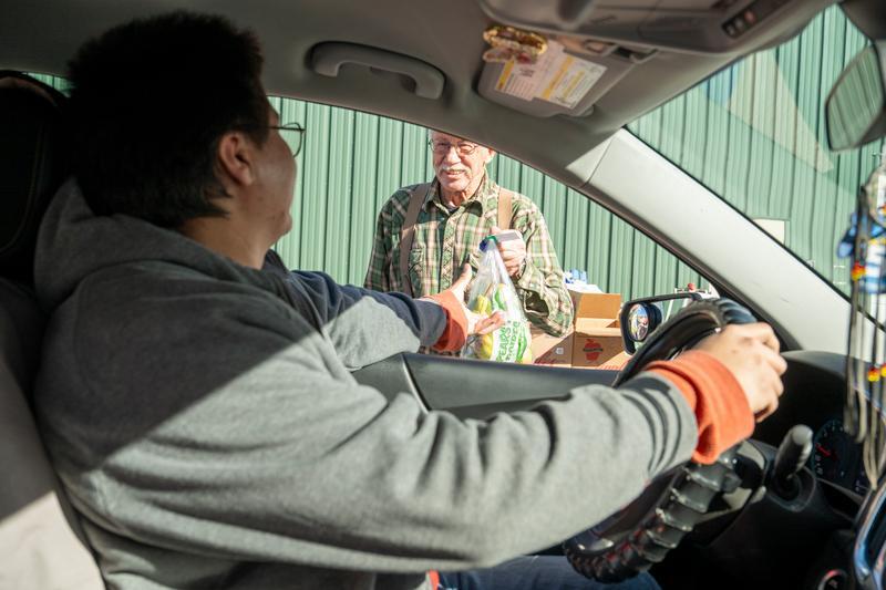 a person handing food through an open car window at a mobile food pantry