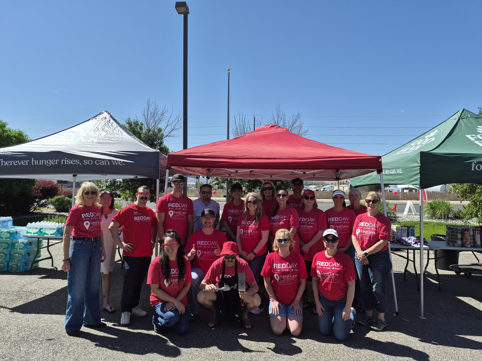 Group of Keller Williams volunteers wearing red shirts standing in front of event tents outside.