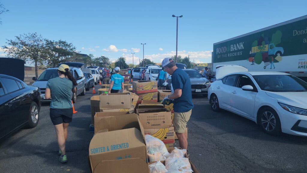 food distribution with volunteers carrying food from boxes to lines of cars.